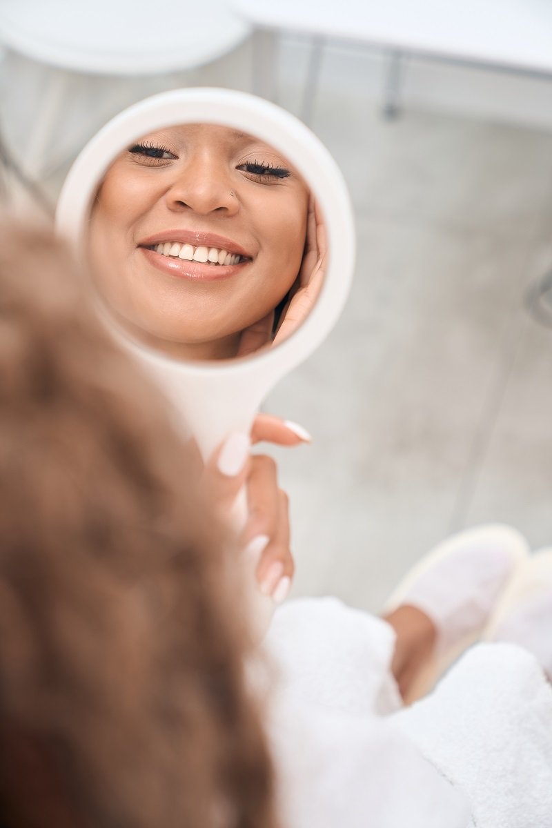 Woman smiling and checking teeth in mirror after dental treatment